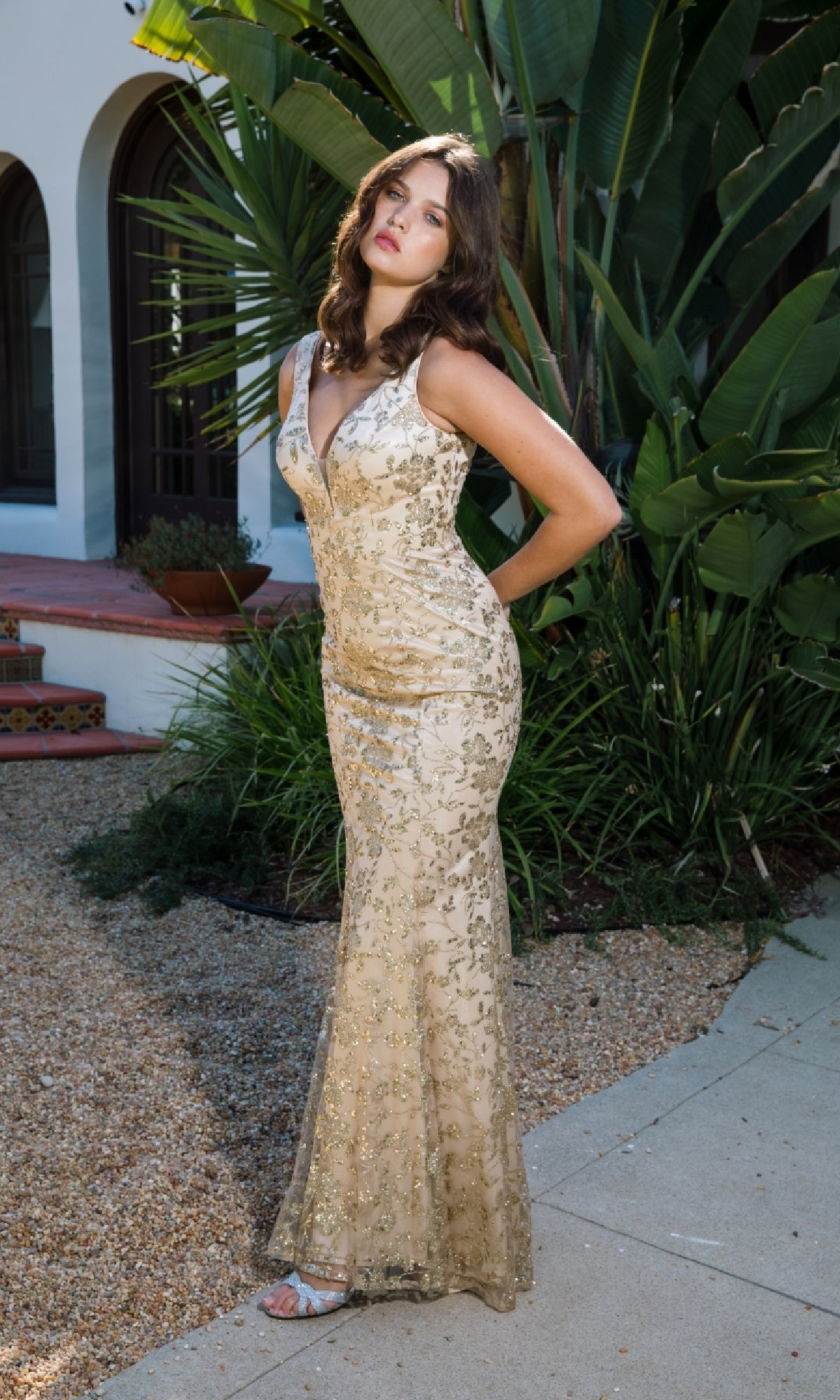 Wearing the Sequin-Print Long Prom Dress: Eureka 9706, a woman poses outdoors on a pathway with hands behind her back, surrounded by lush green plants.